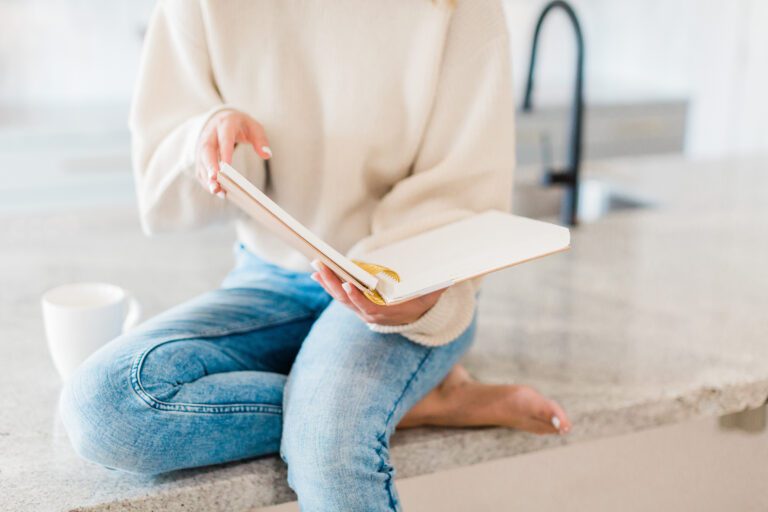 A woman sitting on a counter, with a cup of coffee and looking through a planner