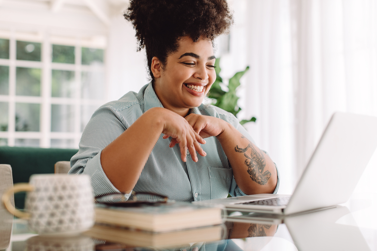 A woman with curly hair sitting at a table, working on her laptop.