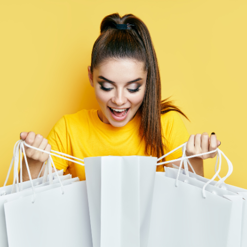 A happy woman with shopping bags on a yellow background. She seems excited about her purchases!